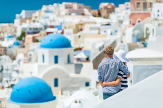 A couple enjoying the scenic view of white buildings and blue domes in Santorini, Greece, symbolizing relocation and new beginnings for international citizens.