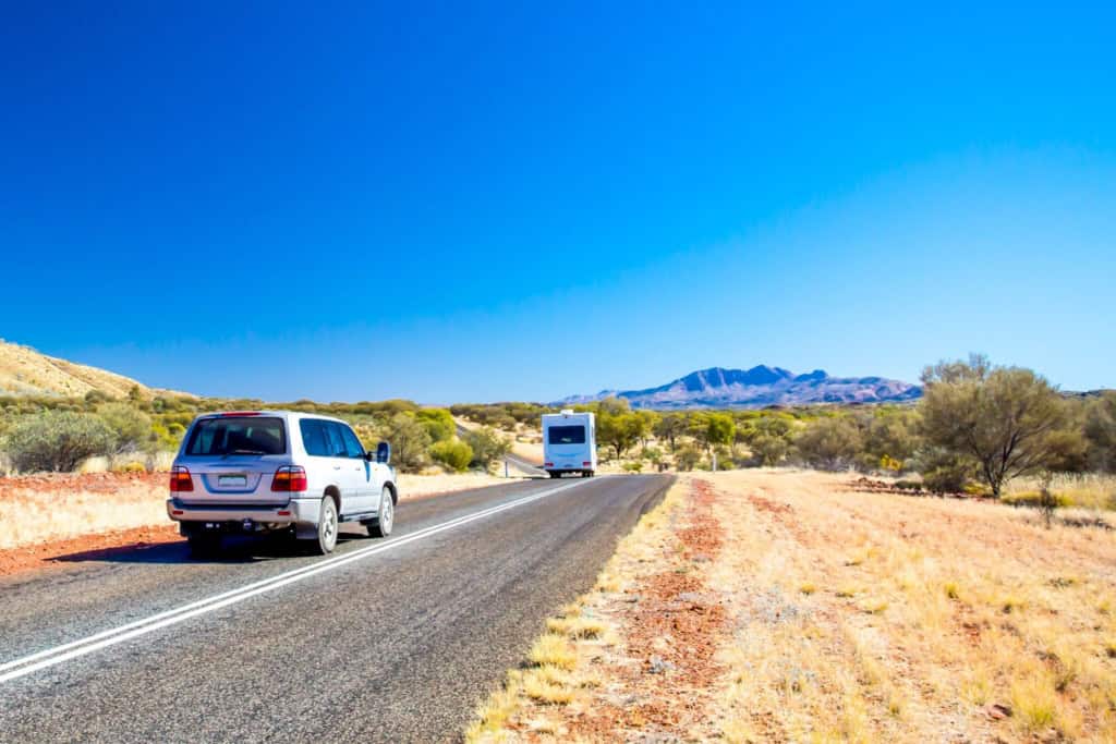 Expat driving on a remote Australian road with scenic desert landscape and mountains in the background.