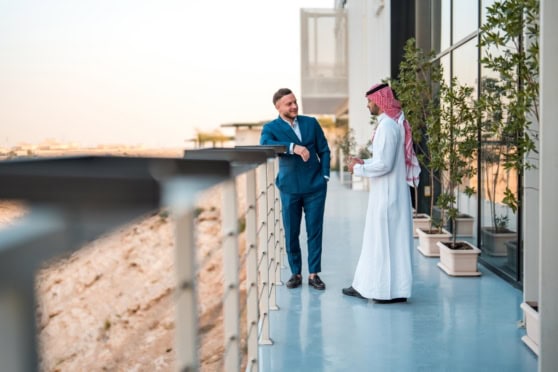 Business professionals engaging in a conversation on a modern balcony in Saudi Arabia, highlighting expatriate work opportunities and international insurance solutions.