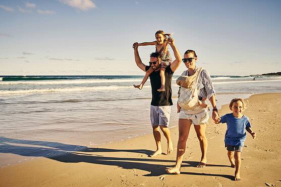 Family enjoying a day at the beach in Australia, with children and parents walking along the shoreline during sunset.