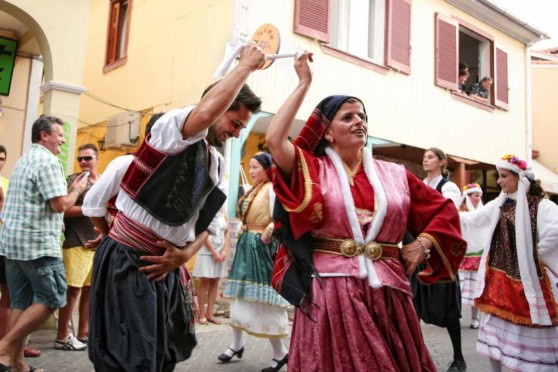 Traditional Greek dance, featuring dancers in colorful costumes performing in a lively street scene.