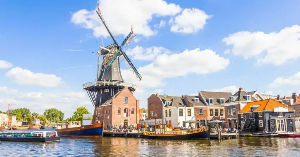 Windmill and traditional Dutch houses along a canal in the Netherlands, illustrating the country's iconic landscape and cost of living considerations for international residents.