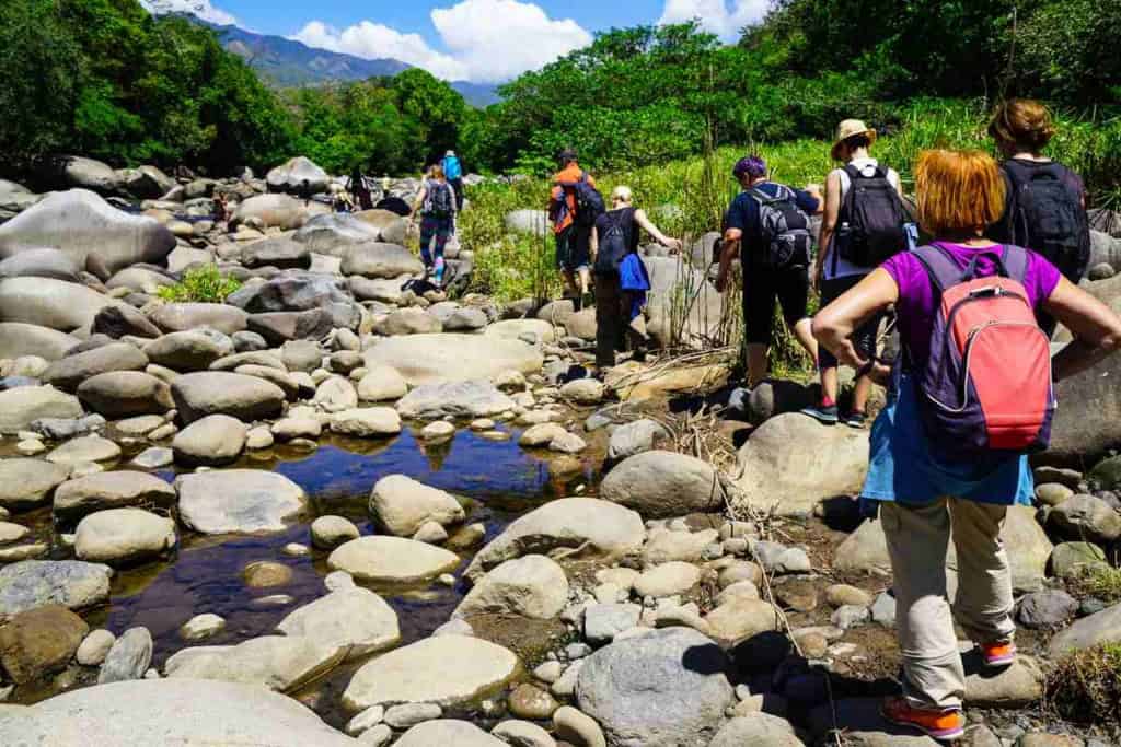 Group of tourists hiking across rocky riverbed in Boquete, Panama, one of the best places to retire in Panama, surrounded by lush greenery and mountains, showcasing outdoor adventure and exploration.