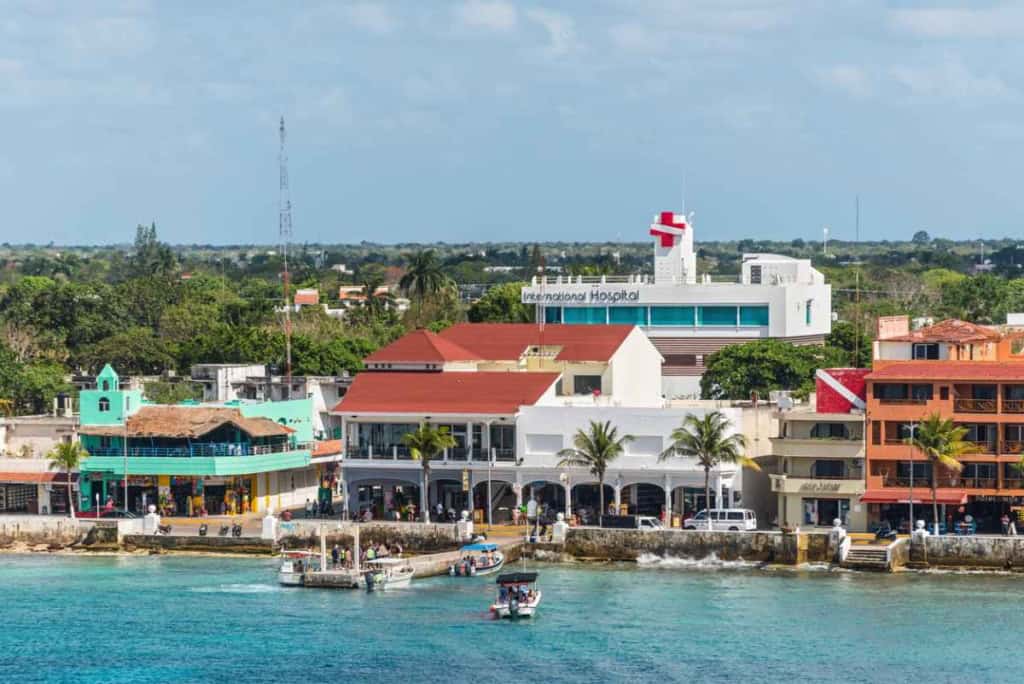 Coastal view of a Mexican town with colorful buildings, a hospital, and boats on the water, illustrating the vibrant lifestyle for Americans relocating to Mexico.