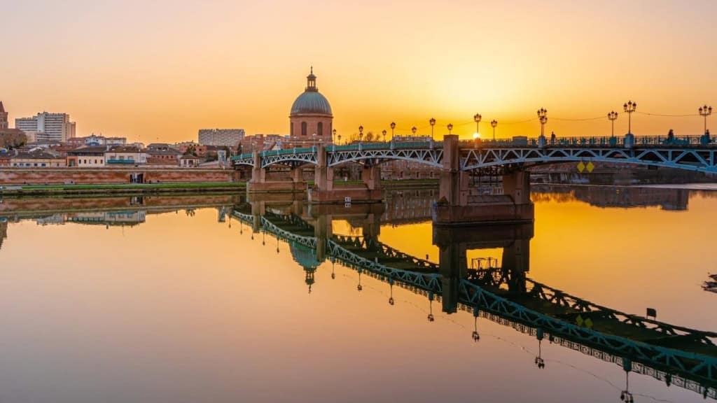 Scenic view of a French city at sunset, featuring a river, bridge, and historic architecture, ideal for expats considering relocation or travel to France.