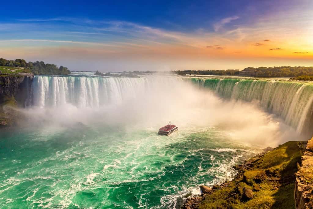 Scenic view of Niagara Falls during sunset with a boat in the foreground and vibrant sky, highlighting the natural beauty and appeal of living abroad.