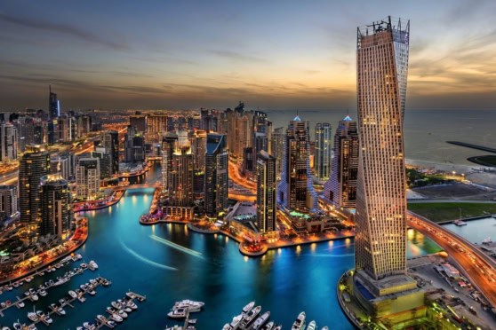 Aerial view of Dubai Marina with modern skyscrapers and luxury yachts at sunset. The city’s vibrant lights reflect on the water, showcasing a bustling urban landscape and iconic architecture.