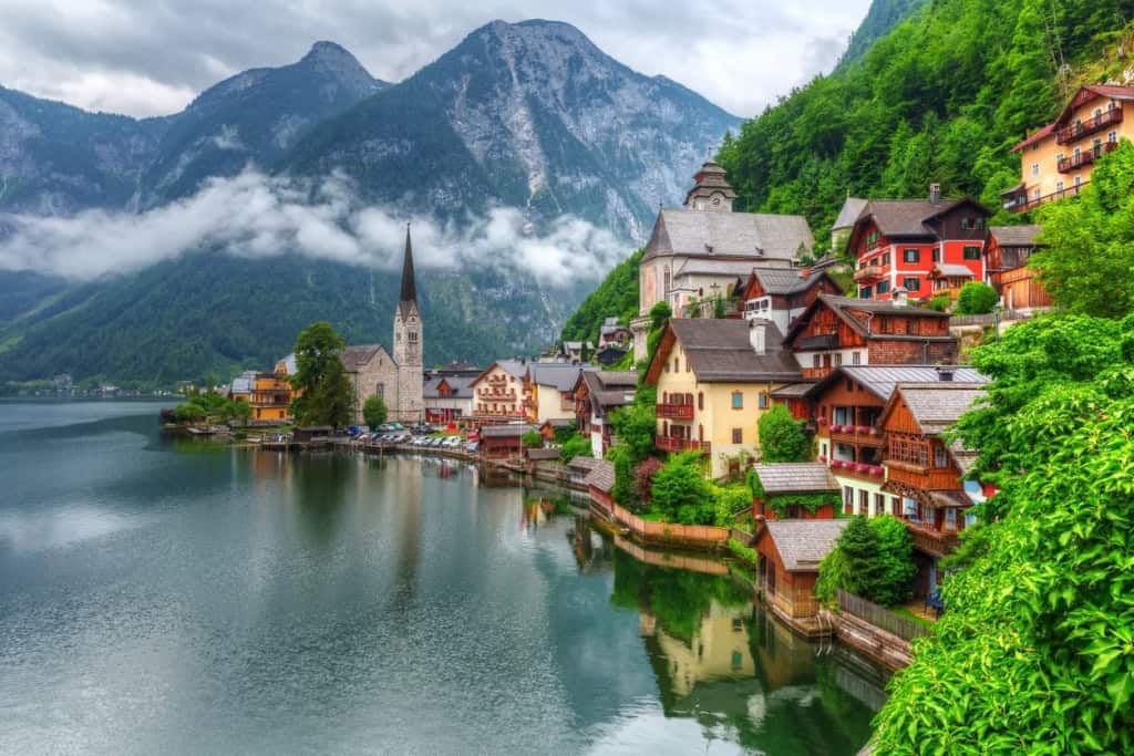 Beautiful alpine village nestled along a serene lake with colorful houses, a historic church, and lush green mountains in the background.