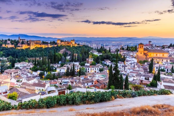 Panoramic view of a historic Spanish town with white buildings, lush greenery, and a castle at sunset, highlighting the safest places to live in Spain.