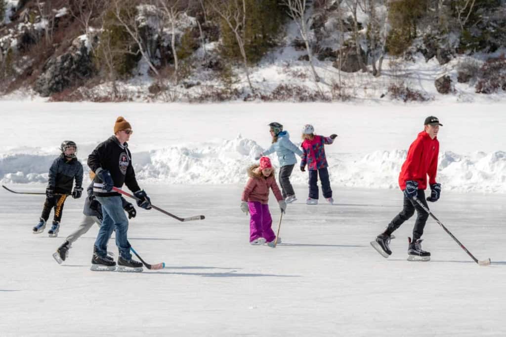 Family enjoying ice skating on a frozen lake with children and adults in winter clothing.