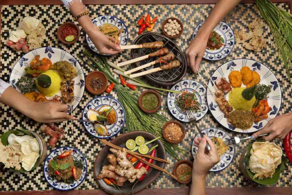 A vibrant spread of Indonesian dishes including satay, rice, vegetables, and fried snacks served on patterned plates, showcasing Indonesia's rich culinary culture.