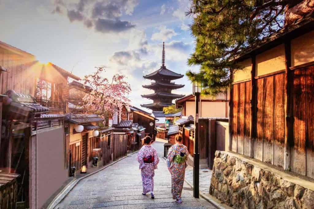 Traditional Japanese street scene with two women in kimonos walking towards a pagoda.