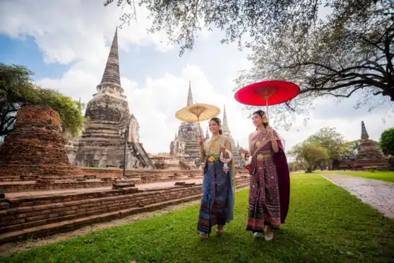 Thai women in traditional dress holding umbrellas at historic temple site.