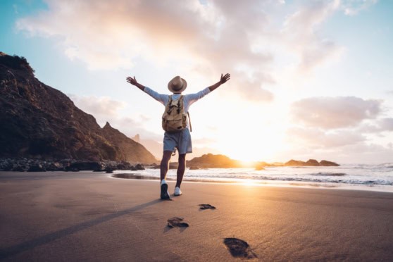 A traveler on a beach at sunset with arms raised, symbolizing freedom and adventure for Americans living abroad.