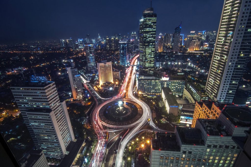 Aerial view of a vibrant cityscape featuring tall buildings, bright lights, and bustling traffic, perfect for illustrating international relocation or urban living.