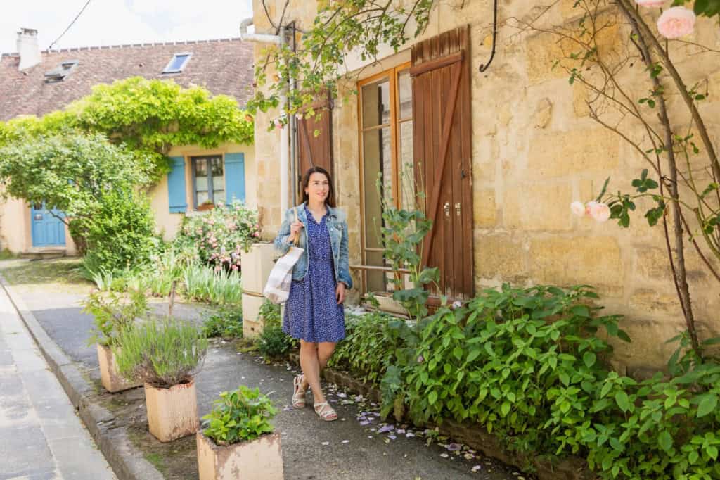 Woman walking along a charming French street with rustic houses and lush greenery, symbolizing expatriation and new beginnings in France.