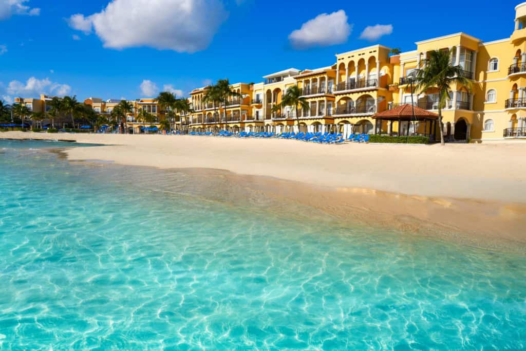 Beautiful beach with clear turquoise waters and luxurious resort buildings in the background.