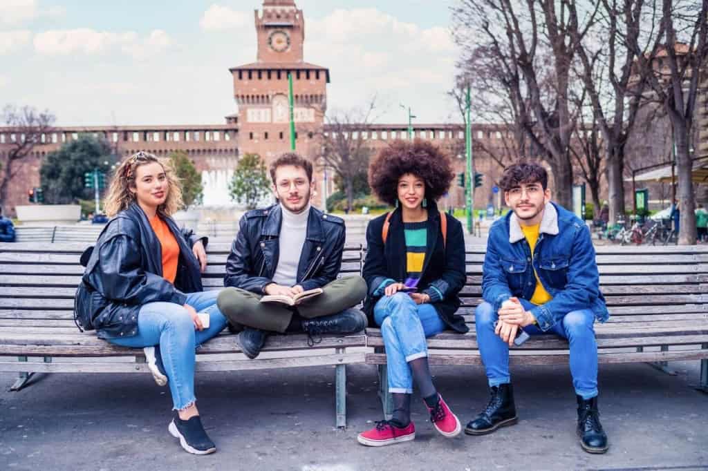 Expat friends relaxing in a park in Italy, enjoying the cityscape and historic architecture in the background.