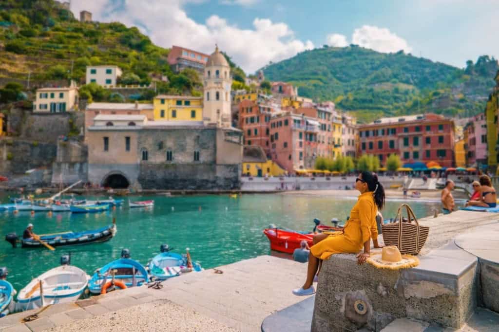 Expat enjoying a scenic harbor in Italy with colorful buildings and boats, highlighting the vibrant lifestyle and cost of living considerations for international residents.