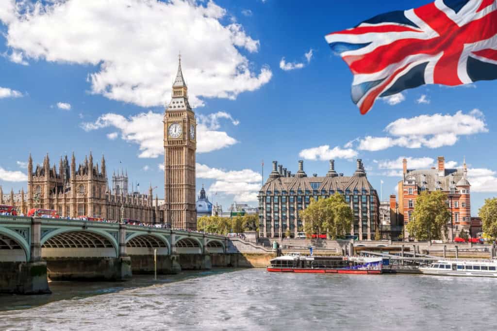 Iconic view of London's Big Ben, Houses of Parliament, and Westminster Bridge with the Union Jack flag flying in the foreground.