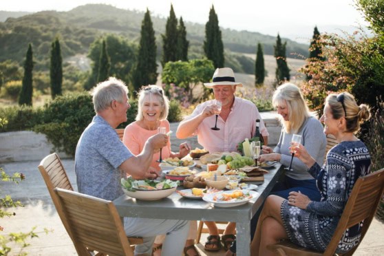 Group of seniors enjoying a meal outdoors in a scenic Italian garden, highlighting retirement in Italy and international health insurance options.