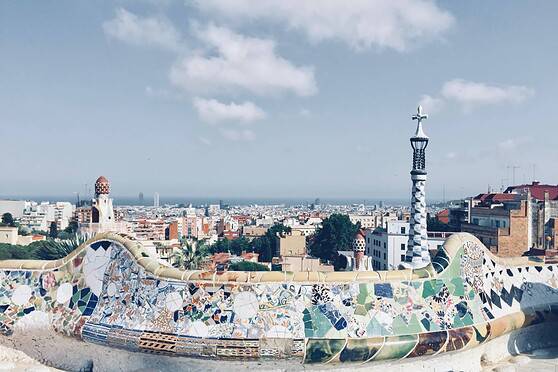 Barcelona cityscape featuring the colorful mosaic benches of Park Güell, designed by Antoni Gaudí, overlooking the urban skyline and the Mediterranean Sea in the background.