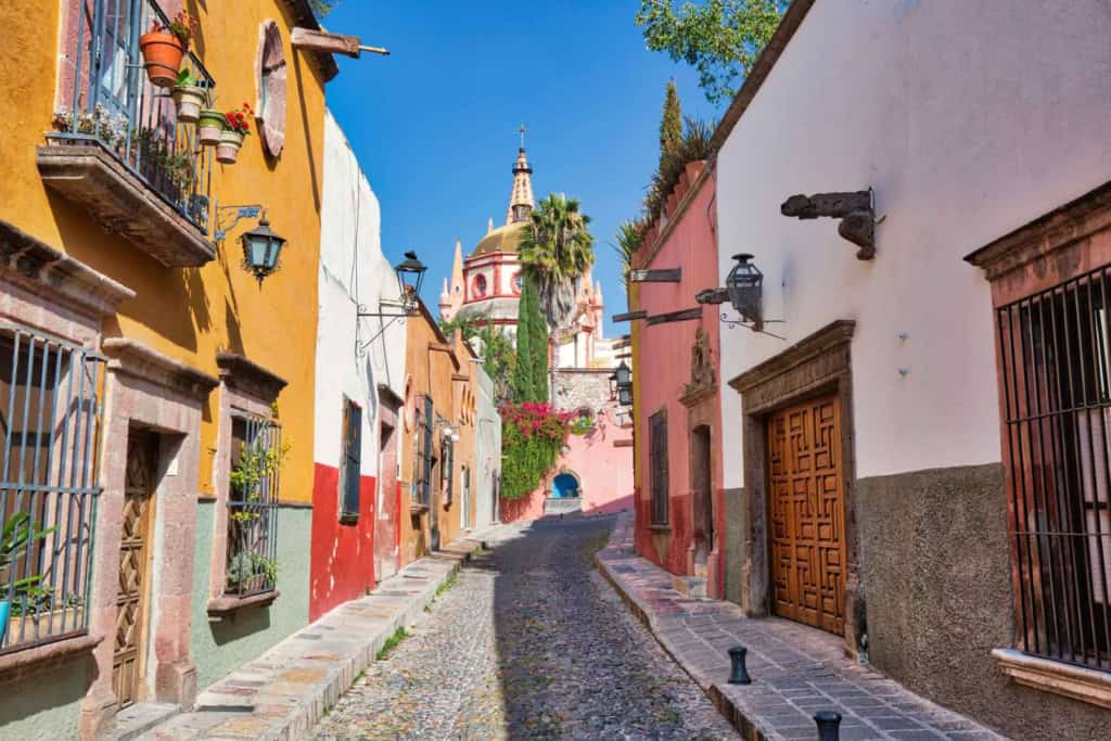An image of a charming, colorful street in Mexico featuring traditional architecture and a visible church in the background, highlighting the country's vibrant culture and safe living environments.