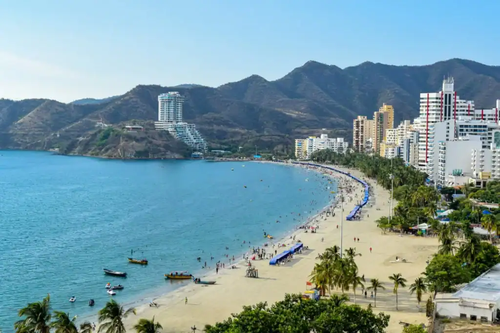 Scenic view of a Colombian beach with high-rise buildings, mountains, and clear blue water, ideal for expatriates considering relocation.