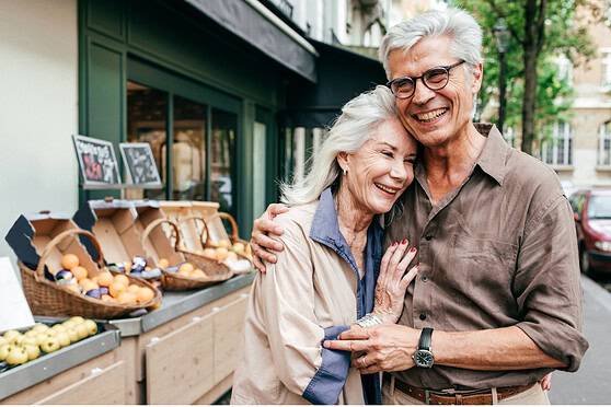 A joyful elderly couple embracing outdoors in front of a market stall, symbolizing retirement and enjoying life in France.