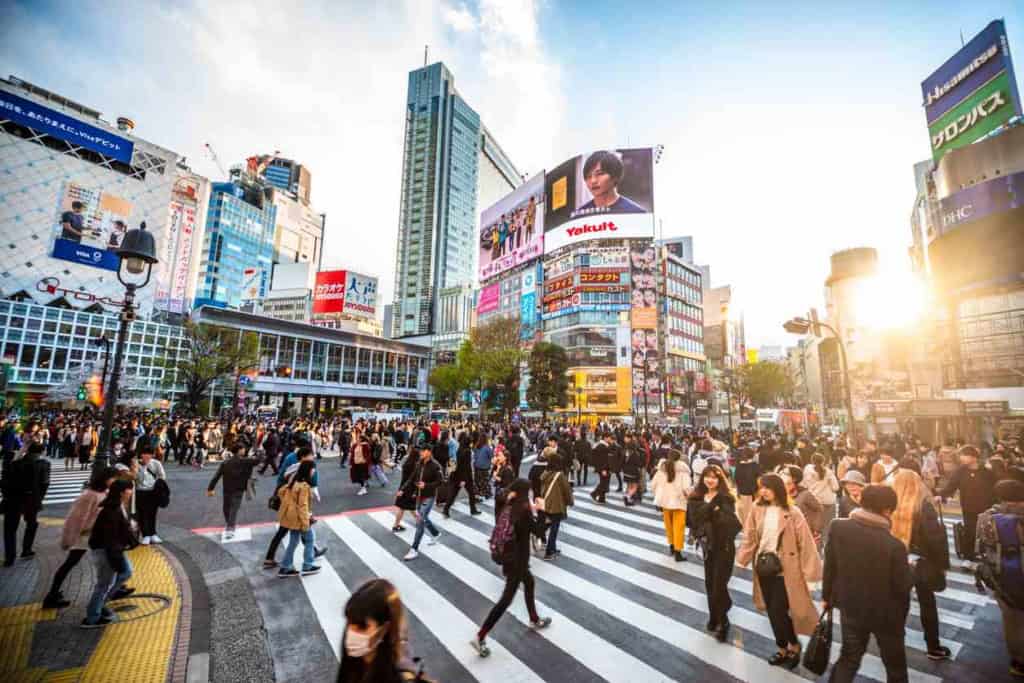 A busy Shibuya crossing in Tokyo with hundreds of pedestrians crossing the street amidst towering buildings and vibrant billboards.