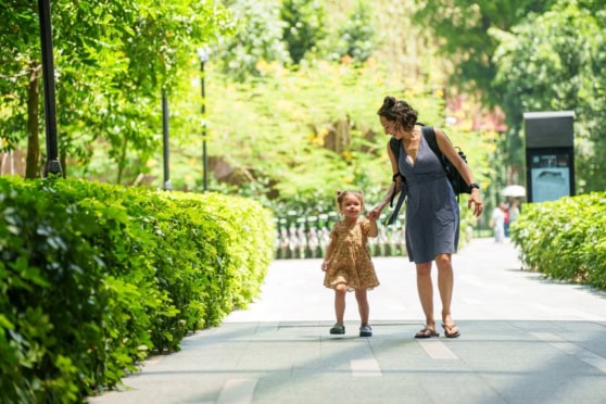 Woman and young girl walking hand in hand in a lush, green park in Singapore, enjoying a sunny day. Perfect for families relocating to Singapore and seeking health insurance options.