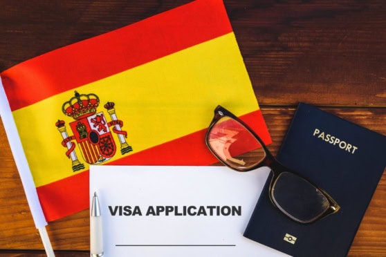 Spanish flag alongside a visa application form, passport, and sunglasses, symbolizing international travel and immigration processes for Spanish citizens.
