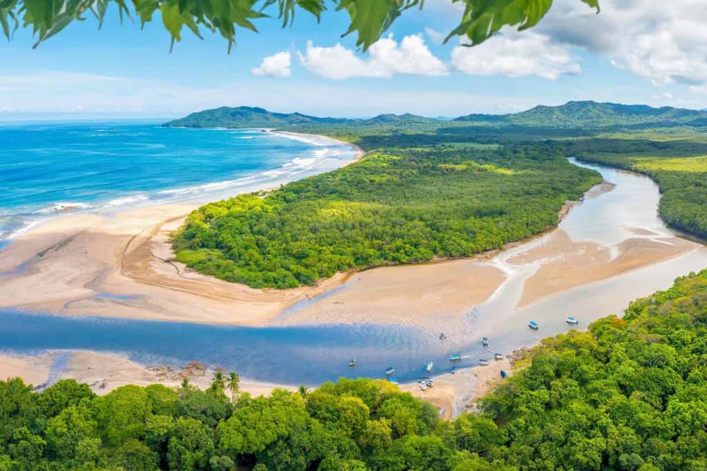 An aerial view of Costa Rica's lush coastline featuring a river delta, sandy beaches, and vibrant green forests under a bright blue sky.
