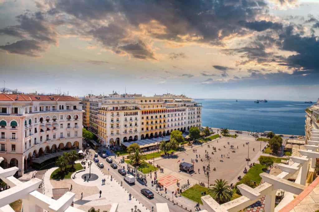 Beautiful view of a Greek city square with historic buildings and the sea in the background.