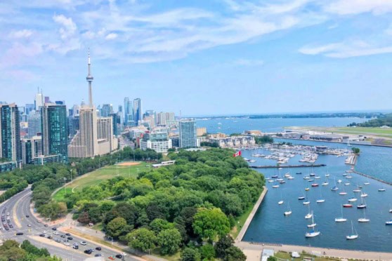 Aerial view of Toronto's skyline, CN Tower, and Toronto Harbour with sailboats and lush green parks on a clear day.