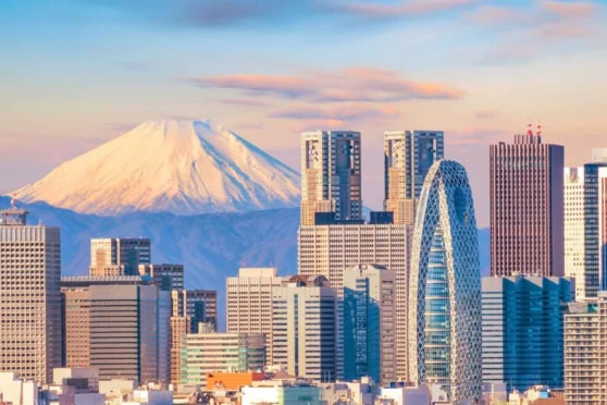 Modern Tokyo cityscape with iconic skyscrapers and Mount Fuji behind during sunset.
