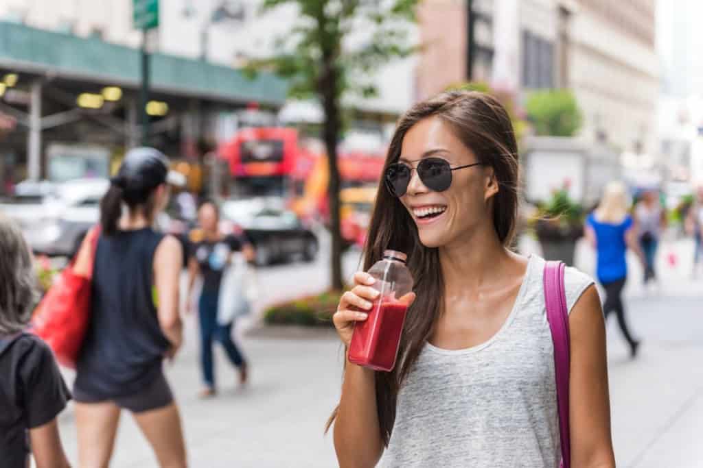 Happy woman enjoying a drink on a busy city street, representing the cost of living in the U.S. with a vibrant urban background.