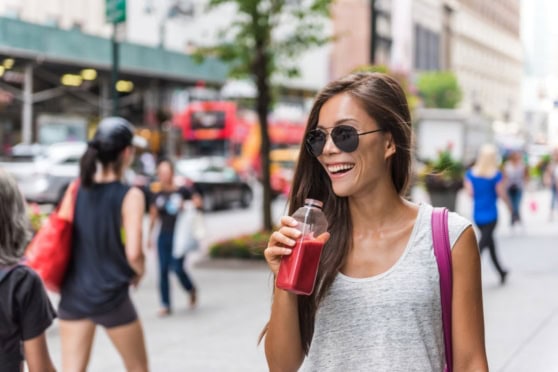 Happy woman enjoying a drink on a busy city street, representing the cost of living in the U.S. with a vibrant urban background.