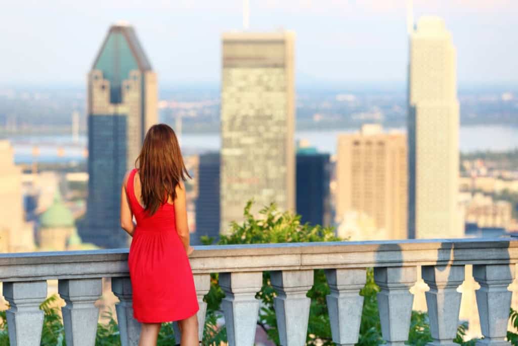 A woman in a red dress overlooking a city skyline from a balcony.