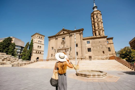 A woman with a hat taking a photo of historic buildings in Spain.