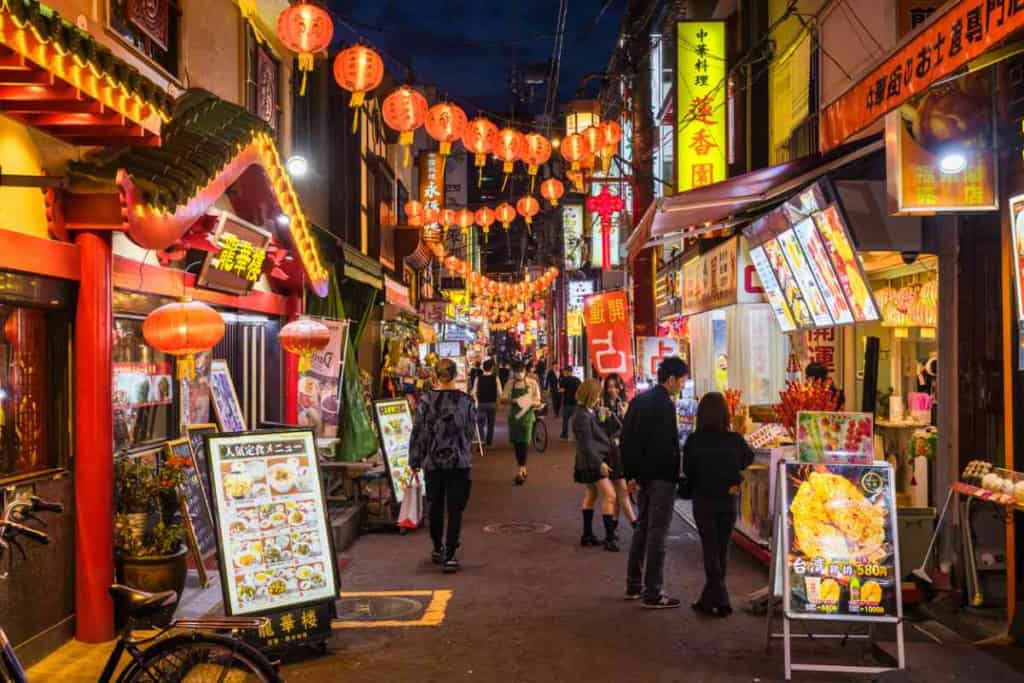 A vibrant night scene in a busy Japanese street with colorful lanterns and illuminated shop signs.
