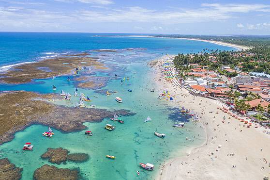 An aerial view of a tropical beach in Brazil with clear turquoise waters, boats, and a lively shoreline.