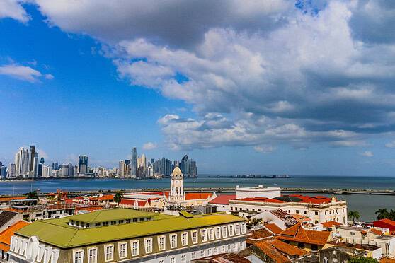 Panoramic view of a modern city skyline along the waterfront with historic and contemporary buildings under a partly cloudy sky.