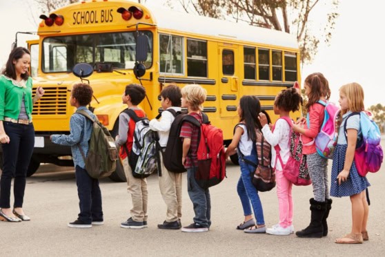 Group of children boarding a yellow school bus with a female teacher or parent supervising, emphasizing school transportation safety.