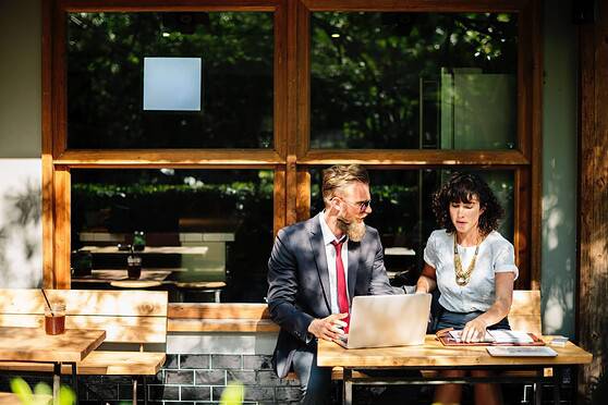 Two professionals discussing insurance options at an outdoor café, with a laptop and documents, representing international insurance services for global citizens.