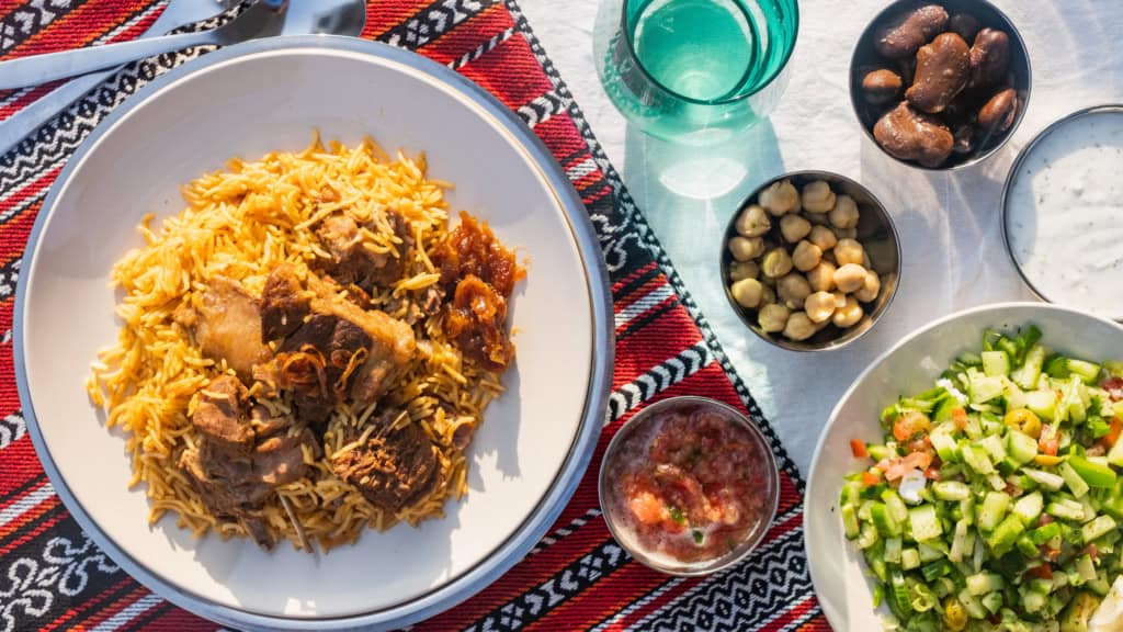 Delicious lamb and rice dish served with fresh salad and side dishes on a patterned tablecloth. Perfect for a hearty meal.