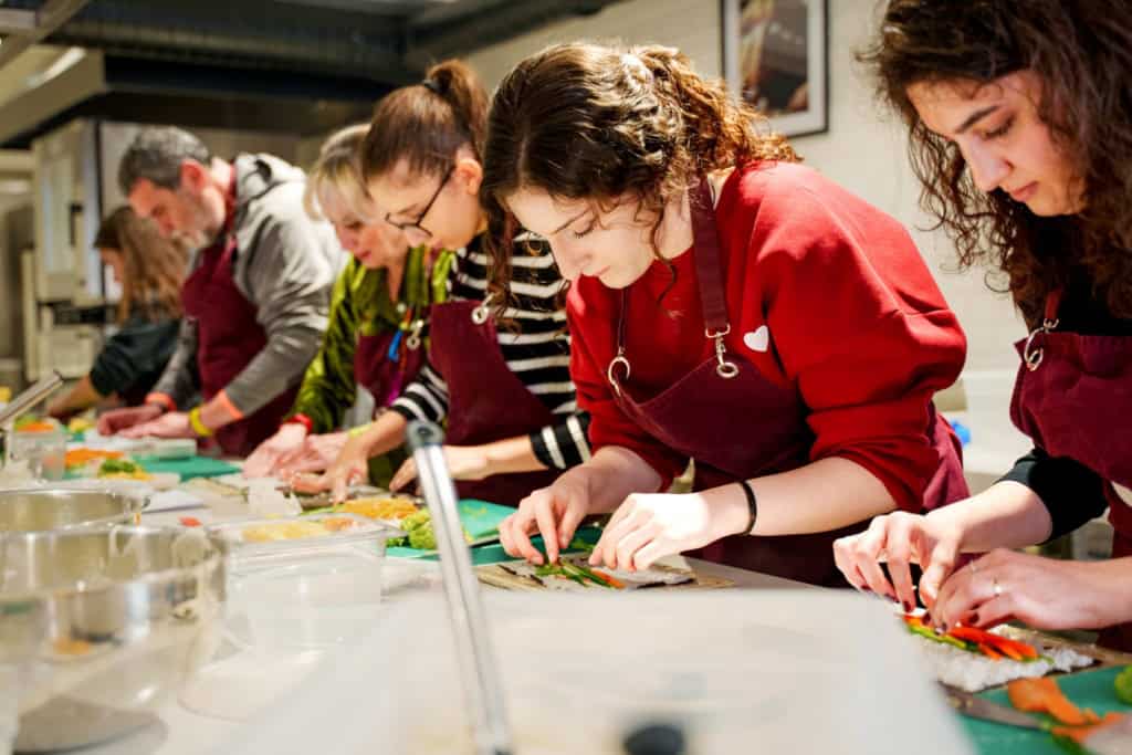 Group of people participating in a sushi-making class, focusing on rolling and preparing sushi in a professional kitchen setting.