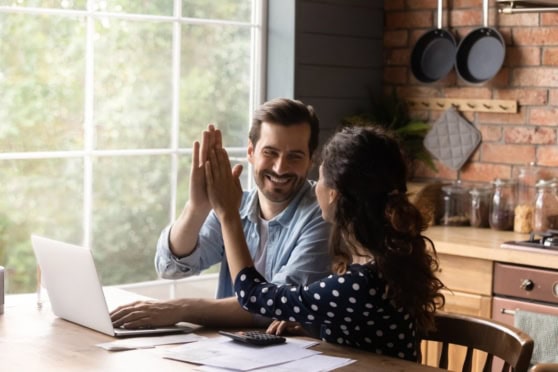 Two diverse individuals high-fiving in a cozy kitchen, representing international insurance services and global community support.