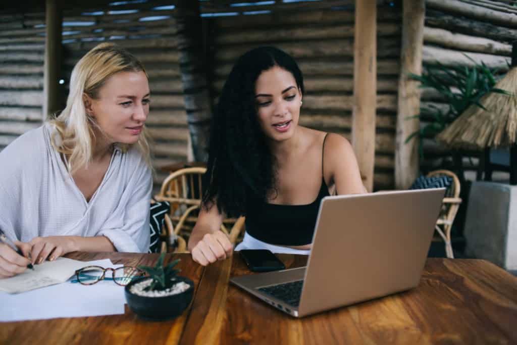 An image of two women discussing insurance options on a laptop at a cozy, rustic setting, representing international insurance services for global citizens.