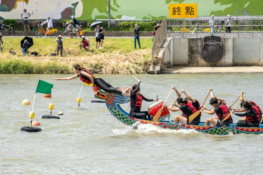 Dragon boat race during a summer festival on a river with spectators on the bank.
